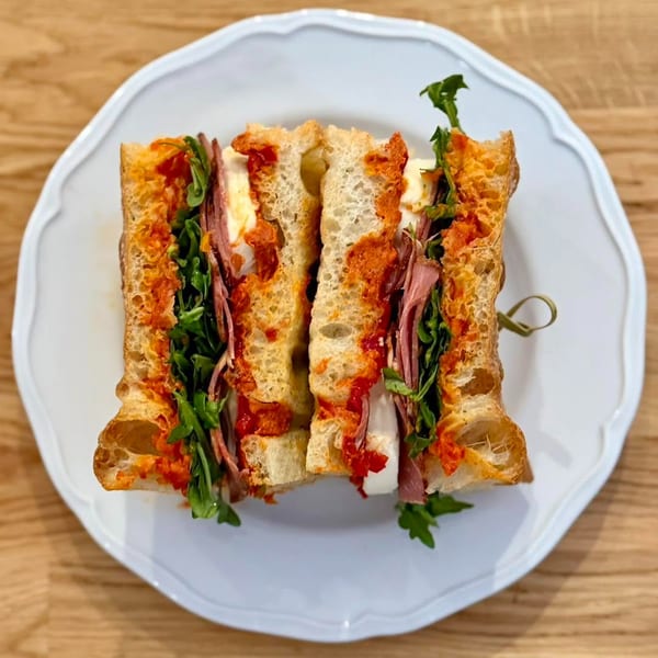 Two halves of a sandwich with meat, cheese, arugula, and red sauce on a white plate.