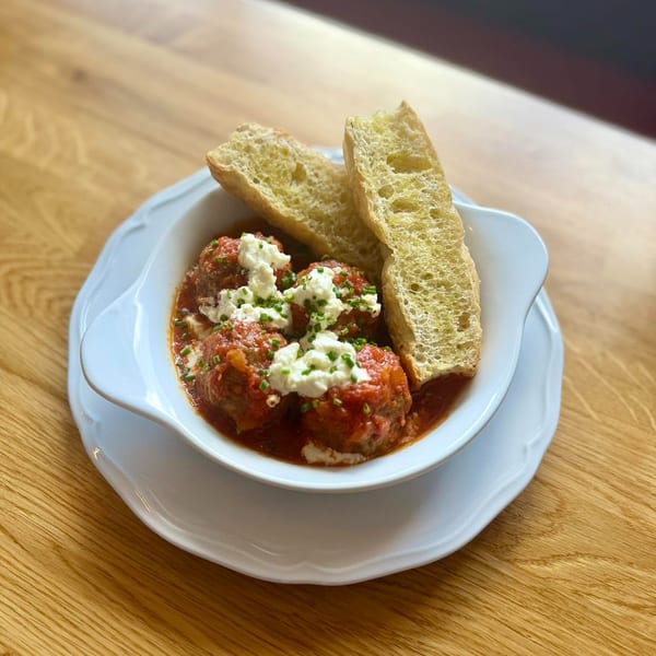Meatballs in red sauce topped with white cheese and chives, served with toasted bread slices.