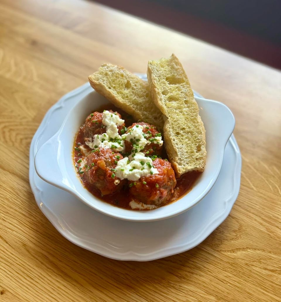 Meatballs in red sauce topped with white cheese and chives, served with toasted bread slices.