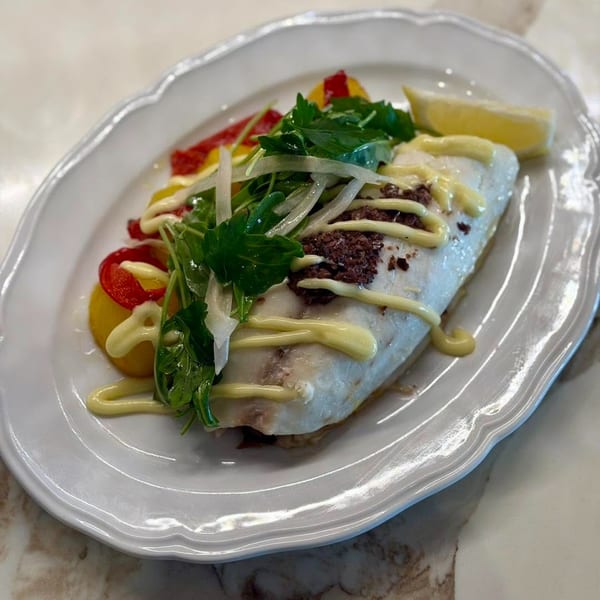 White fish fillet with olive tapenade, mayonnaise drizzle, herbs, bell peppers, and a lemon wedge.