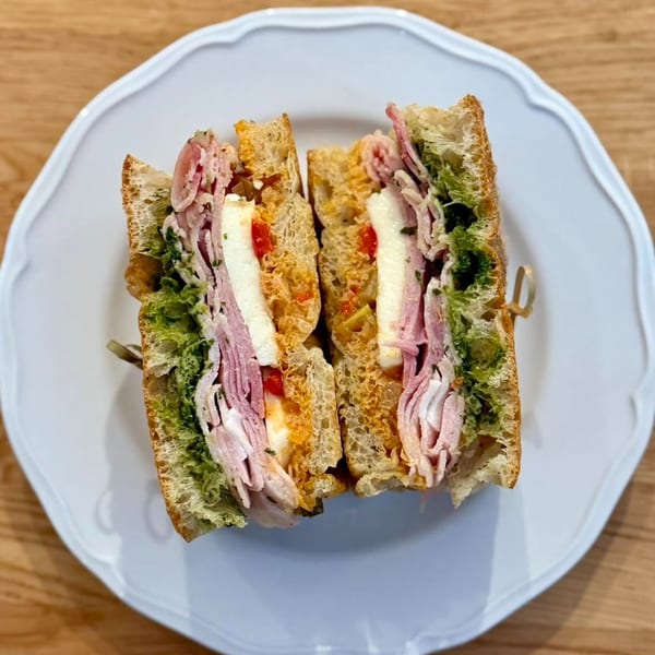 A sliced sandwich with ham, cheese, pesto, and red peppers on a white plate.