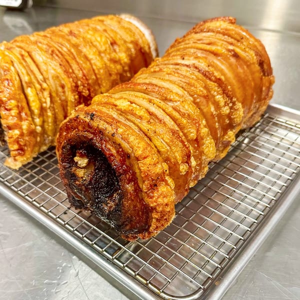 Two crispy, golden-brown rolled pork belly roasts with crackling skin on a metal cooling rack.