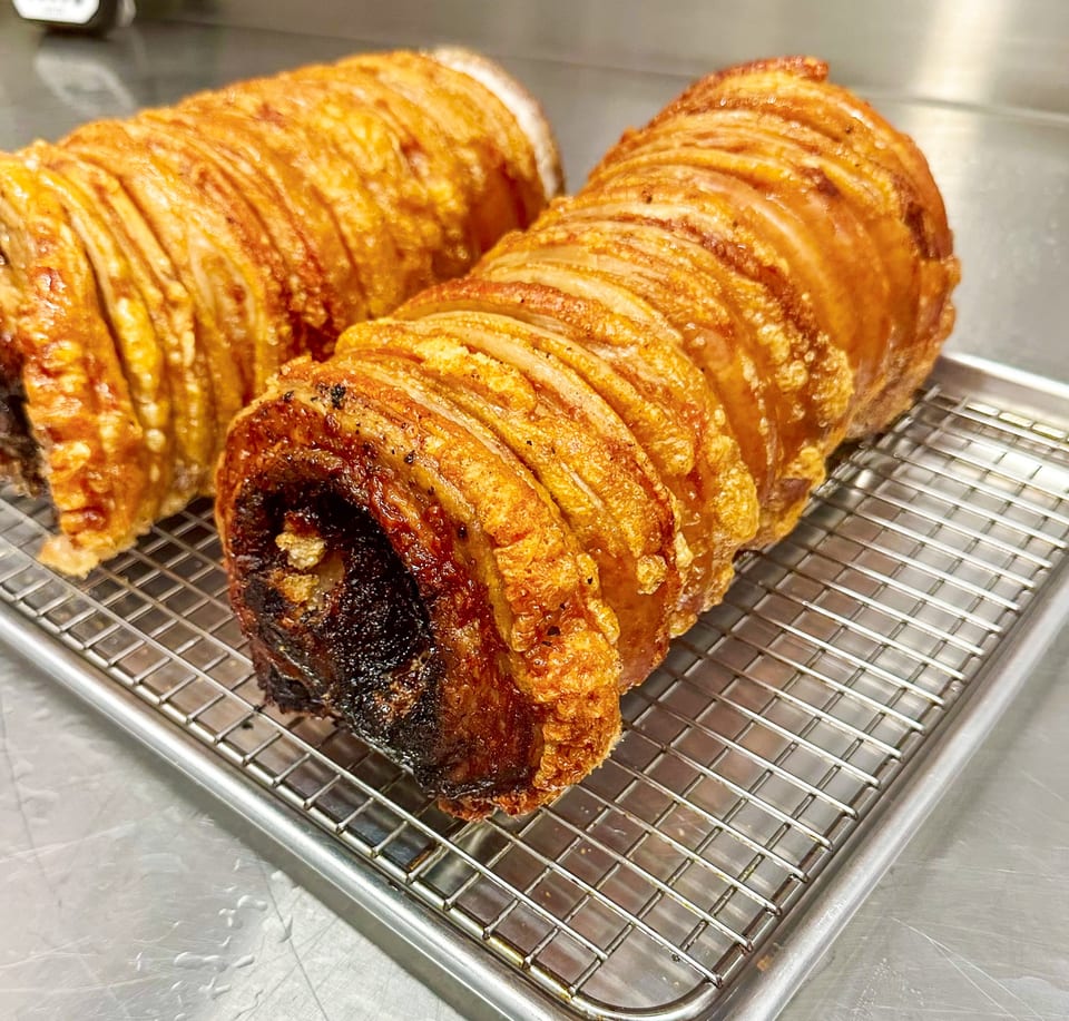 Two crispy, golden-brown rolled pork belly roasts with crackling skin on a metal cooling rack.