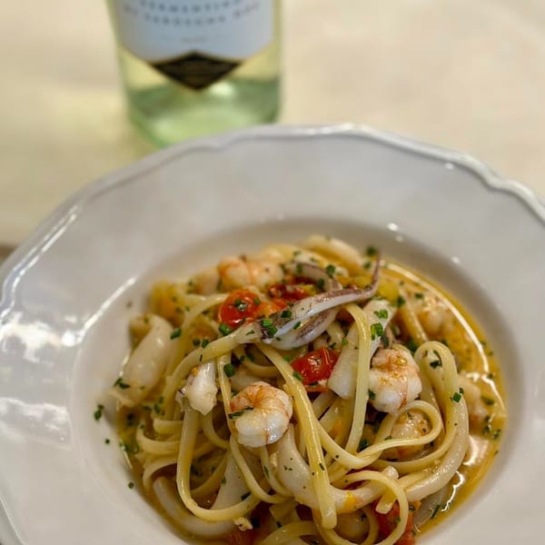 Seafood linguine with shrimp, squid, cherry tomatoes, and herbs, with a bottle of white wine.
