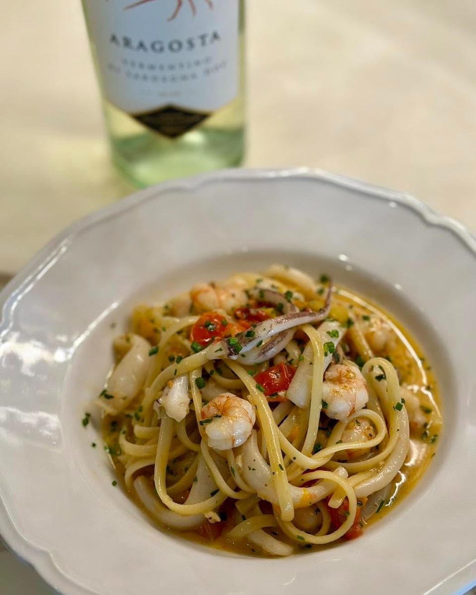 Seafood linguine with shrimp, squid, cherry tomatoes, and herbs, with a bottle of white wine.