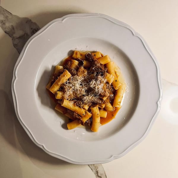 Rigatoni pasta with a rich meat sauce and grated Parmesan cheese on a white scalloped plate.